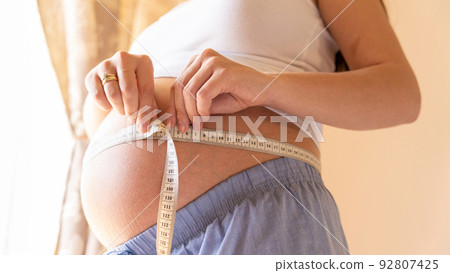 Belly size pregnancy woman measure. Happy young pregnant woman with tape measuring belly. Therapy, healthcare, motherhood concept. 92807425