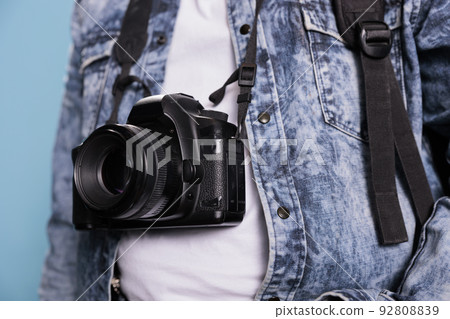 Close up shot of photographer wearing denim jacket and having modern photo device. Photography enthusiast having professional DSLR camera while standing on blue background. Studio shot 92808839