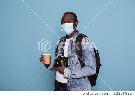 Professional photographer wearing virus protection facemask and having camera while going on vacation trip. Man with DSLR device and protective mask wearing backpack while enjoying urban cityscape. 92808880