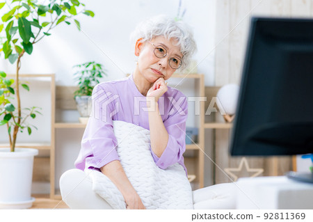 Senior woman thinking while watching TV Senior woman thinking while watching TV 92811369