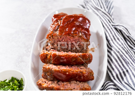 Slicing classic meatloaf with a sweet glaze on a white serving plate 92812176