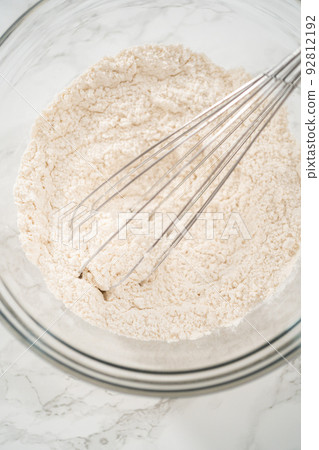 Mixing ingredients in a large glass mixing bowl to bake banana oatmeal muffins. Mixing ingredients in a large glass mixing bowl to bake banana oatmeal muffins. 92812192