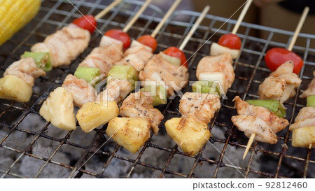 Happy family making a Barbecue on charcoal fire wood at the backyard. Mother and daughters enjoy a BBQ party at backyard. Happy family making a Barbecue on charcoal fire wood at the backyard. Mother and daughters enjoy a BBQ party at backyard. 92812460