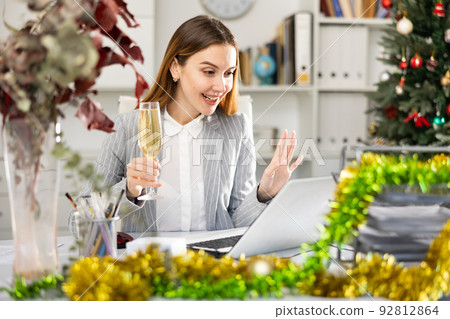 Woman manager with glass of champagne having video call conversation in Christmas decorated office 92812864
