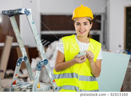 Woman builder writes a message or makes an order for building materials on phone Woman builder writes a message or makes an order for building materials on phone 92813160