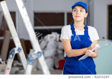 Focused female builder filling out papers at indoor construction site Focused female builder filling out papers at indoor construction site 92813297