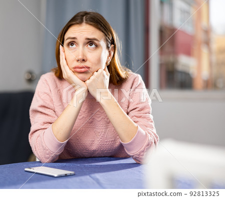 Upset young woman is worried while sitting at table Upset young woman is worried while sitting at table 92813325