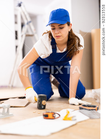Female carpenter using rubber mallet to lay laminate flooring 92813558