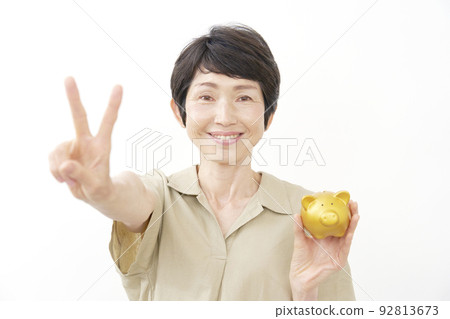 Senior woman holding a piggy bank and making a peace sign White background Senior woman holding a piggy bank and making a peace sign White background 92813673