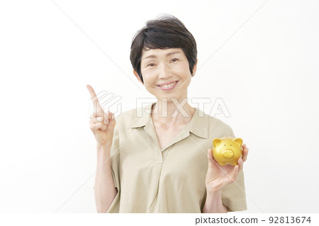 拿著存錢罐並且指向左邊白色背景的一位資深婦女 92813674