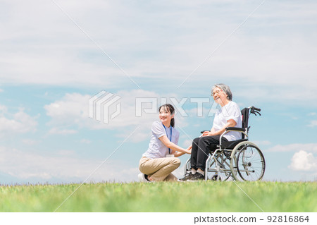 一位在公園散步的護理人員和一位坐在輪椅上的老婦人（藍天） 92816864