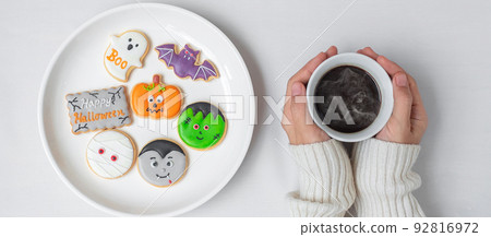 woman hand holding coffee cup during eating funny Halloween Cookies. Happy Halloween day, Trick or Threat, Hello October, fall autumn, Traditional, party and holiday concept woman hand holding coffee cup during eating funny Halloween Cookies. Happy Halloween day, Trick or Threat, Hello October, fall autumn, Traditional, party and holiday concept 92816972