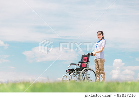 A caregiver/occupational therapist with a wheelchair in the blue sky 92817216