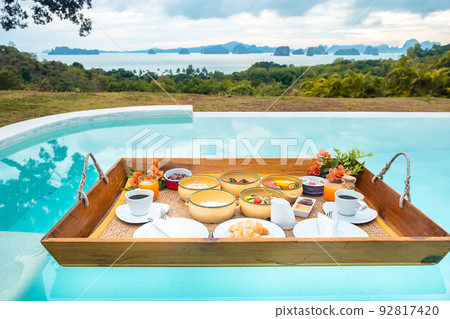 Floating Breakfast tray in swimming pool at luxury hotel or tropical resort villa, fruits, croissant, coffee, and orange juice. Exotic summer, relaxation, tropical travel and vacation concept 92817420