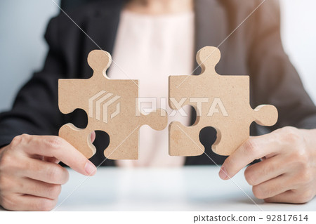 Woman connecting couple puzzle piece, wood jigsaw on table. Business solutions, mission, success, goals and strategy concepts Woman connecting couple puzzle piece, wood jigsaw on table. Business solutions, mission, success, goals and strategy concepts 92817614