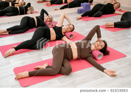 Athletic women doing fascia exercises on the floor with a foam roller massage tool to relieve back tension and relieve muscle pain. The concept of physiotherapy and stretching training Athletic women doing fascia exercises on the floor with a foam roller massage tool to relieve back tension and relieve muscle pain. The concept of physiotherapy and stretching training 92819983