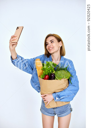 woman hold paper bag with vegetables doing selfie woman hold paper bag with vegetables doing selfie 92820425