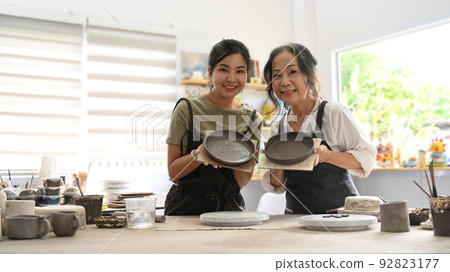 Retired woman and young woman holding handicraft crockery and smiling at camera. Activity, handicraft, hobbies concept 92823177