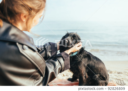 Happy young woman sitting on the beach hugging her black cocker spaniel dog Happy young woman sitting on the beach hugging her black cocker spaniel dog 92826809