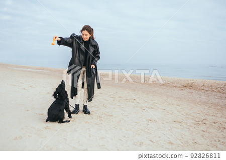 Woman wearing black coat plays with her dog Woman wearing black coat plays with her dog 92826811