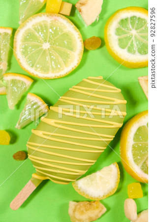Yellow ice cream on a stick, bananas and lemons on a green background, top view Yellow ice cream on a stick, bananas and lemons on a green background, top view 92827596