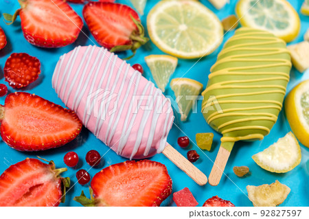 Two ice creams on a sticks - strawberry and lemon on a blue background. Summer fruit desserts. Two ice creams on a sticks - strawberry and lemon on a blue background. Summer fruit desserts. 92827597