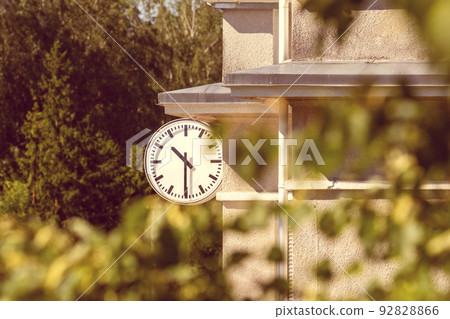 Large clock on the outside of a building seen through a trees Large clock on the outside of a building seen through a trees 92828866