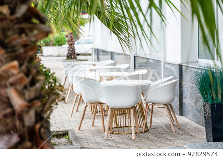 Street cafe with white chairs, green foliage around. Without people, tourism, travel. Street cafe with white chairs, green foliage around. Without people, tourism, travel. 92829573