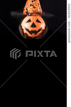 Vertical Happy Halloween black card. A woman in a hat holds a bucket of candy instead of a head. Place for copy space text Vertical Happy Halloween black card. A woman in a hat holds a bucket of candy instead of a head. Place for copy space text 92829932