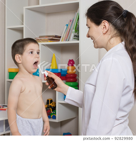 A pediatrician or nurse and a boy 3-4 years old. Throat spray, treatment of pharyngitis, stomatitis or thrush in children. A pediatrician or nurse and a boy 3-4 years old. Throat spray, treatment of pharyngitis, stomatitis or thrush in children. 92829980