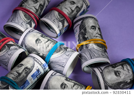 Close-up of Rolled up one hundred dollar bills with rubber bands on purple background Close-up of Rolled up one hundred dollar bills with rubber bands on purple background 92830411