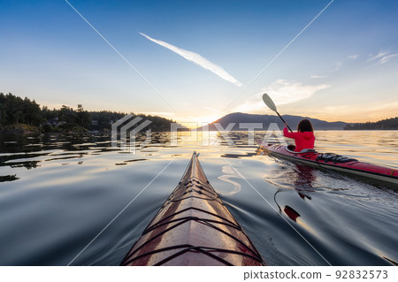 Adventurous Woman on Sea Kayak paddling in the Pacific Ocean. Sunny Summer Sunset Adventurous Woman on Sea Kayak paddling in the Pacific Ocean. Sunny Summer Sunset 92832573