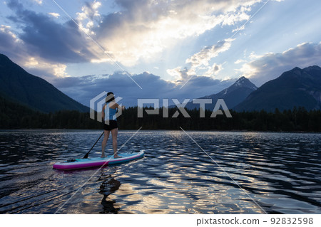 Adventurous Woman Paddle Boarding in a Lake around Canadian Mountain Landscape 92832598