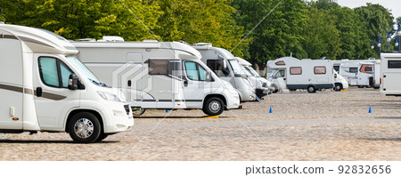 Many white modern campervan recreational motor home vehicles parked in row at camper park site Magdeburg city against Elbe river bridge. Motorhome campground stataion travel destination. RV lifestyle 92832656