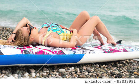 sexy girl is lying on a sup board by the sea in beautiful stylish summer clothes 92832981