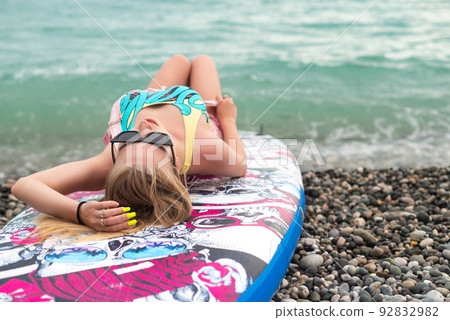 sexy girl is lying on a sup board by the sea in beautiful stylish summer clothes sexy girl is lying on a sup board by the sea in beautiful stylish summer clothes 92832982