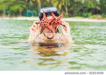 Happy young scuba diver holding sea star, smiling, looking at camera 92833099