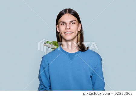 Portrait of young male with green parrot on his shoulder on gray background 92833802