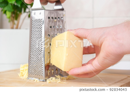 A man rubs cheese on metal grater for freezing and 92834043