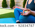 cropped shot of a young woman doing yoga, lotus position, on a mat in the garden. unrecognizable woman doing meditation and breathing exercises. concept of health and well-being. 92834787