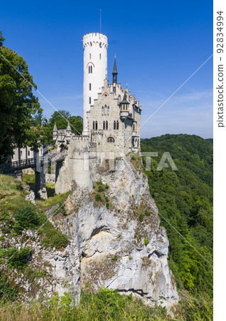 Photo of lichtenstein castle or Schloss on forested rock cliff in Swabian Alps in summer. Seasonal panorama of romantic fairytale palace in Gothic revival style over sky. European famous landmark Photo of lichtenstein castle or Schloss on forested rock cliff in Swabian Alps in summer. Seasonal panorama of romantic fairytale palace in Gothic revival style over sky. European famous landmark 92834994