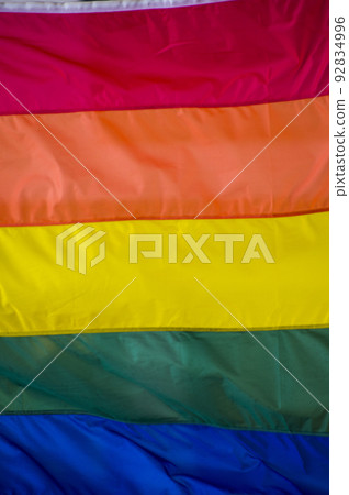 Close-Up rainbow gay pride flag outside on a street. Symbol of the Lesbian Bisexual Transgender LGBT community waving in wind against cloudy sky. Social movement for freedom and equliaty. Copy Space  92834996
