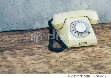 Vintage yellow rotary dial telephone on wooden table in front gray concrete background 92836372