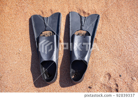 A pair of black flippers on the background of sand next to the water 92839337