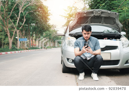 Asian man using mobile phone calling for assistance after a car breakdown on street. Concept of vehicle engine problem or accident and emergency help from Professional mechanic Asian man using mobile phone calling for assistance after a car breakdown on street. Concept of vehicle engine problem or accident and emergency help from Professional mechanic 92839478