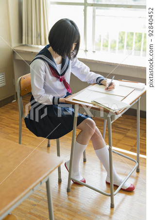 High school girl looking at mobile phone in class High school girl looking at mobile phone in class 92840452