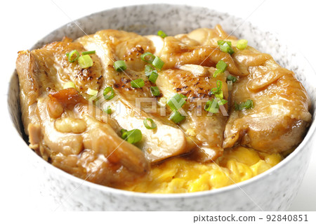A teriyaki chicken bowl with a large piece of chicken on top of an omelet, photographed against a white background 92840851