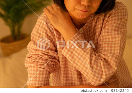 A middle-aged woman wearing pajamas and suffering from stiff shoulders in the bedroom A middle-aged woman wearing pajamas and suffering from stiff shoulders in the bedroom 92842243