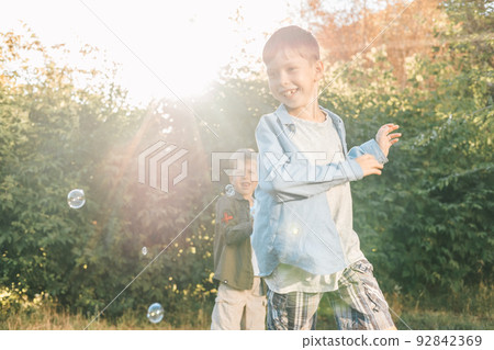 A boy is playing with soap bubbles in a summer park, Among the greenery. A boy is playing with soap bubbles in a summer park, Among the greenery. 92842369