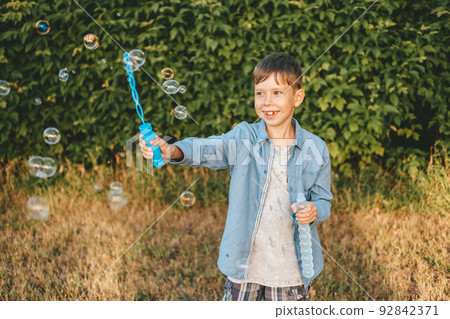A boy is playing with soap bubbles in a summer park, Among the greenery. 92842371